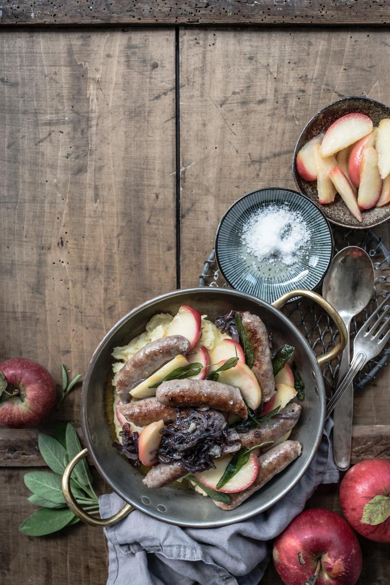 Rezeptbild: softer kartoffelstampf, gebratene apfelspalten mit apfelessig, rote butterzwiebeln, fenchel salsiccia und frittierter salbei